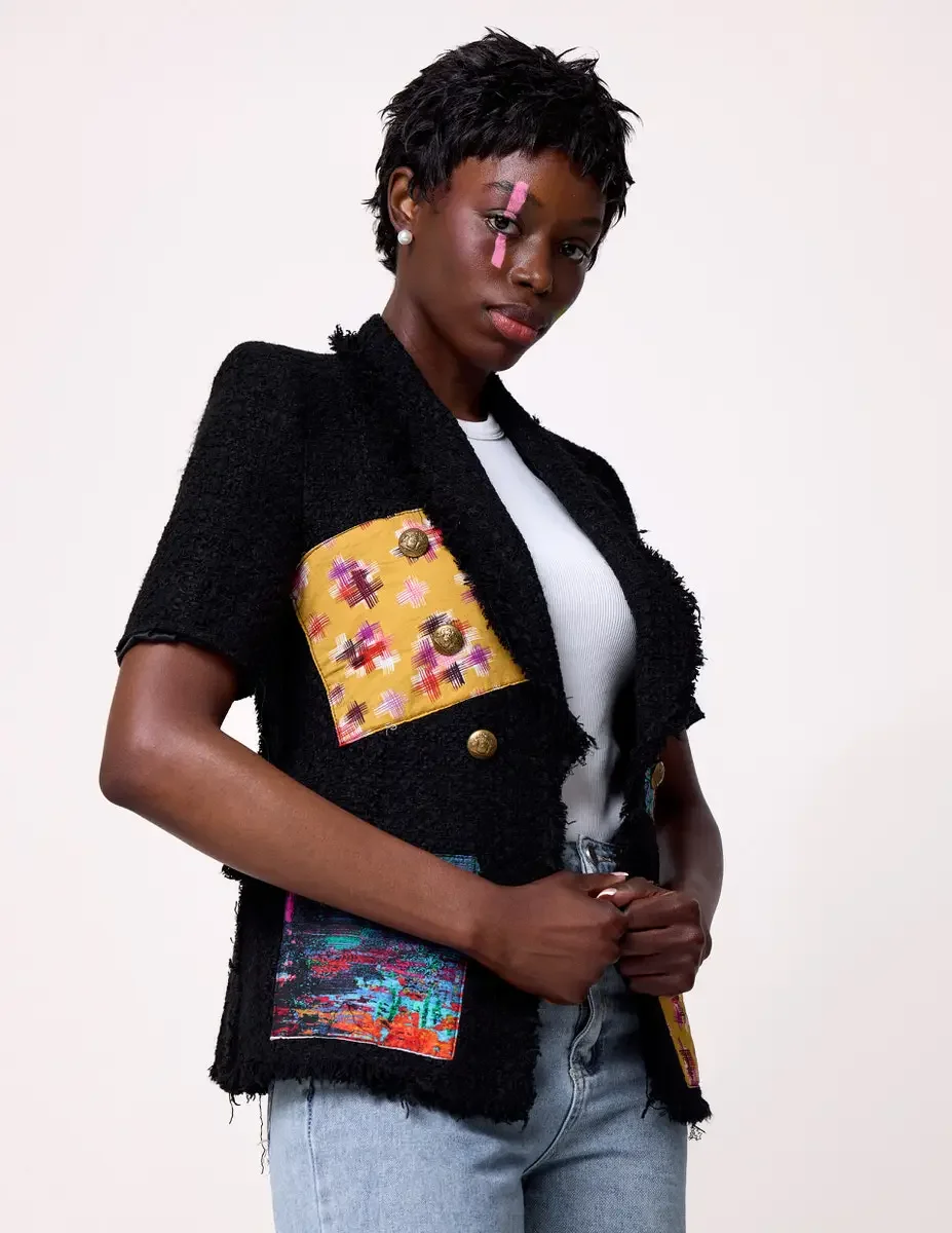 JUS10H Black Summer Jacket editorial, three-quarter detail of black tweed jacket with yellow ikat and multicolor patchwork panels and gold buttons, white tee, light-wash jeans, white background, photographed by Scott Parker Photo