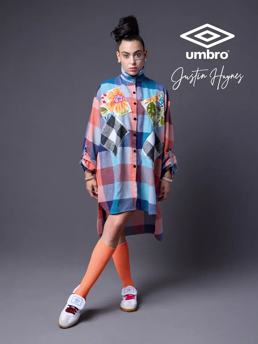 Refined football style for the Umbro France collection. Vanessa standing in a relaxed three-quarter stance in an oversized multicolor plaid shirt dress with floral patchwork panels and orange football knee socks, styled by Justin Haynes, photographed