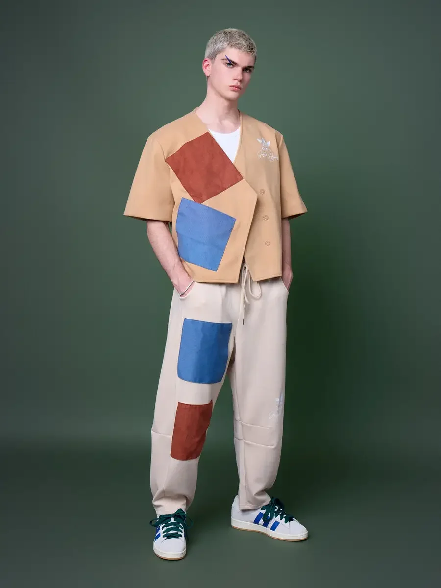 JUS10H x Adidas Brasil campaign, full-length standing shot, tan patchwork short-sleeve vest with terracotta and blue suede panels over cream wide-leg patchwork trousers, Adidas Campus 00s in white with blue stripes and dark green laces, forest green 