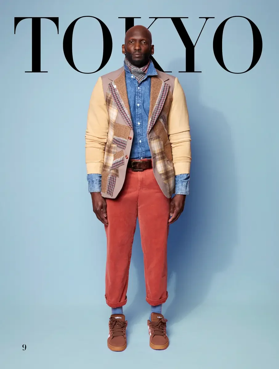 JUS10H 2025 Tokyo lookbook, tan and camel patchwork blazer with tartan panels over denim shirt and rust corduroy trousers with Adidas sneakers, light blue background, photographed by Scott Parker Photo for the Tokyo Fashion Council
