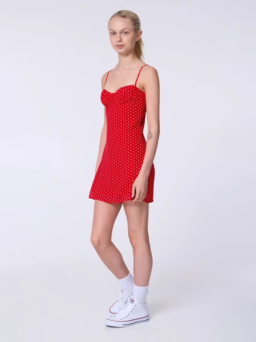 Model portfolio development session, commercial look, red polka dot sweetheart mini dress with spaghetti straps, full-length, three-quarter turn, arms at sides, neutral expression, polka dot mini dress shown against clean background without cardigan,