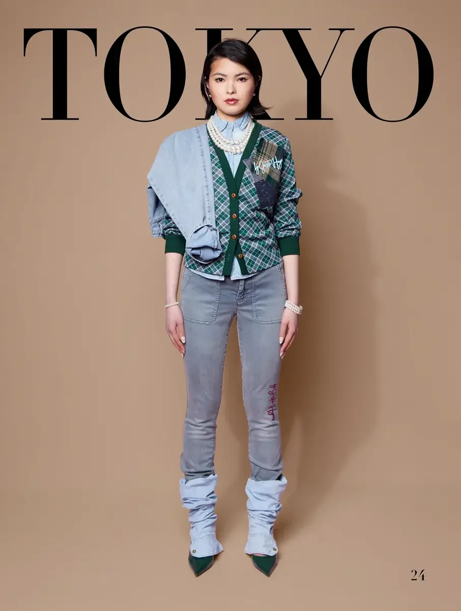 JUS10H 2025 Tokyo lookbook, forest green ribbed cardigan with tartan patch and bow over white shirt and olive mini skirt with tartan patch and fishnet knee socks with Adidas sneakers, light blue background, photographed by Scott Parker Photo for the 