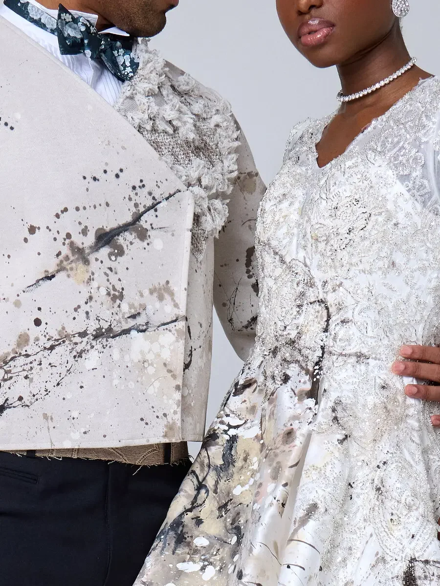 JUS10H 2025 New York Bridal Fashion Week, detail of ivory abstract paint-splatter tuxedo jacket with dark teal floral bow tie alongside white beaded lace ball gown with V-neckline and diamond choker, photographed by Scott Parker Photo