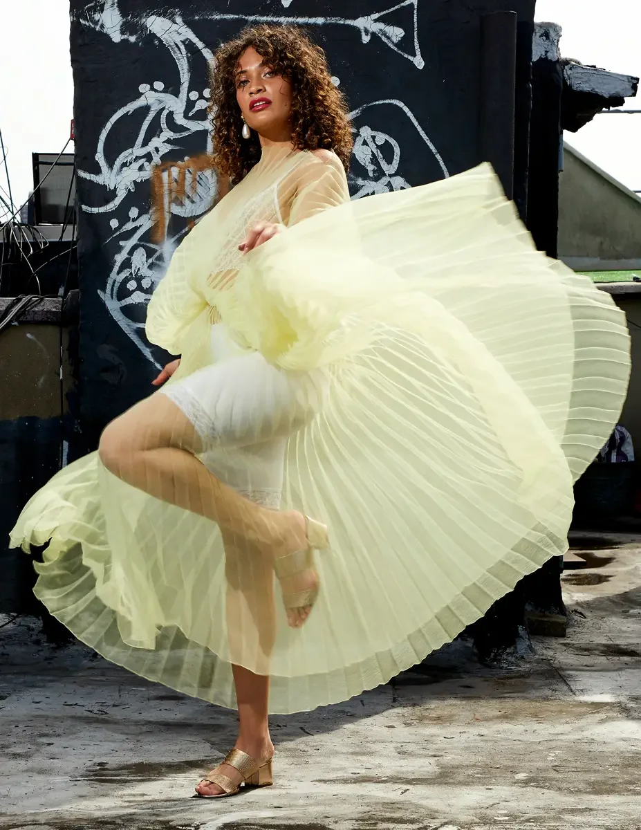 Fashion test shoot, model Ireland T in J'Amemme yellow pleated sheer gown, skirt sweeping wide, graffiti wall backdrop, East Village rooftop, New York City, styling by Matsine Stinson, makeup by Stefani Paige Vivian, photographed by Scott Parker Phot