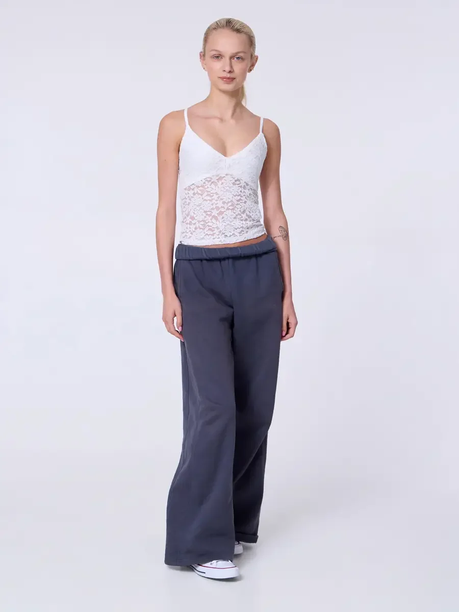 Model portfolio development session, commercial look, white lace crop camisole top and wide-leg charcoal sweatpants with elastic waistband, full-length, facing camera, arms relaxed, composed neutral expression, clean presentation of the lace-to-sweat