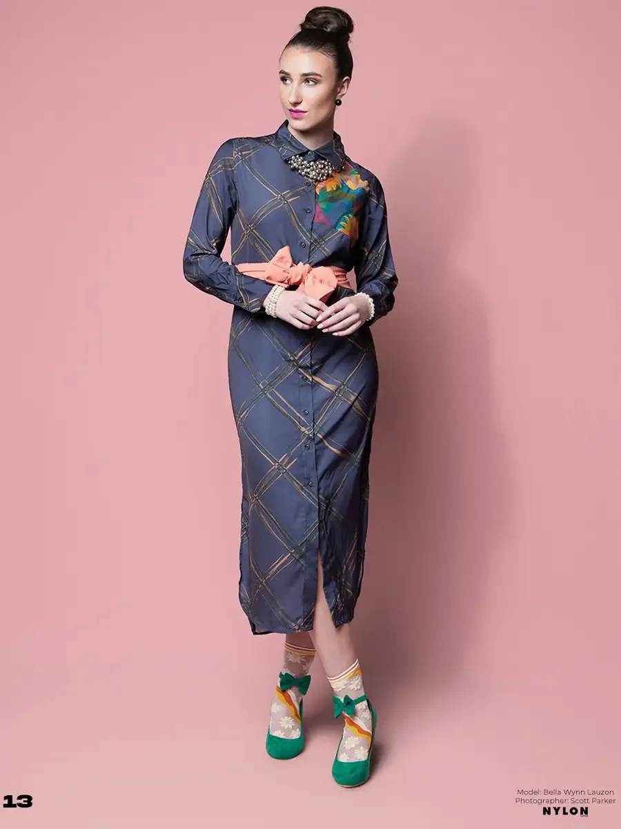 JUS10H 2025 Nylon Japan feature, model in slate blue plaid silk shirtdress with floral patchwork panel and coral bow belt, pearl bracelet, daisy-print sheer socks and green suede Mary Janes, pink background, photographed by Scott Parker Photo