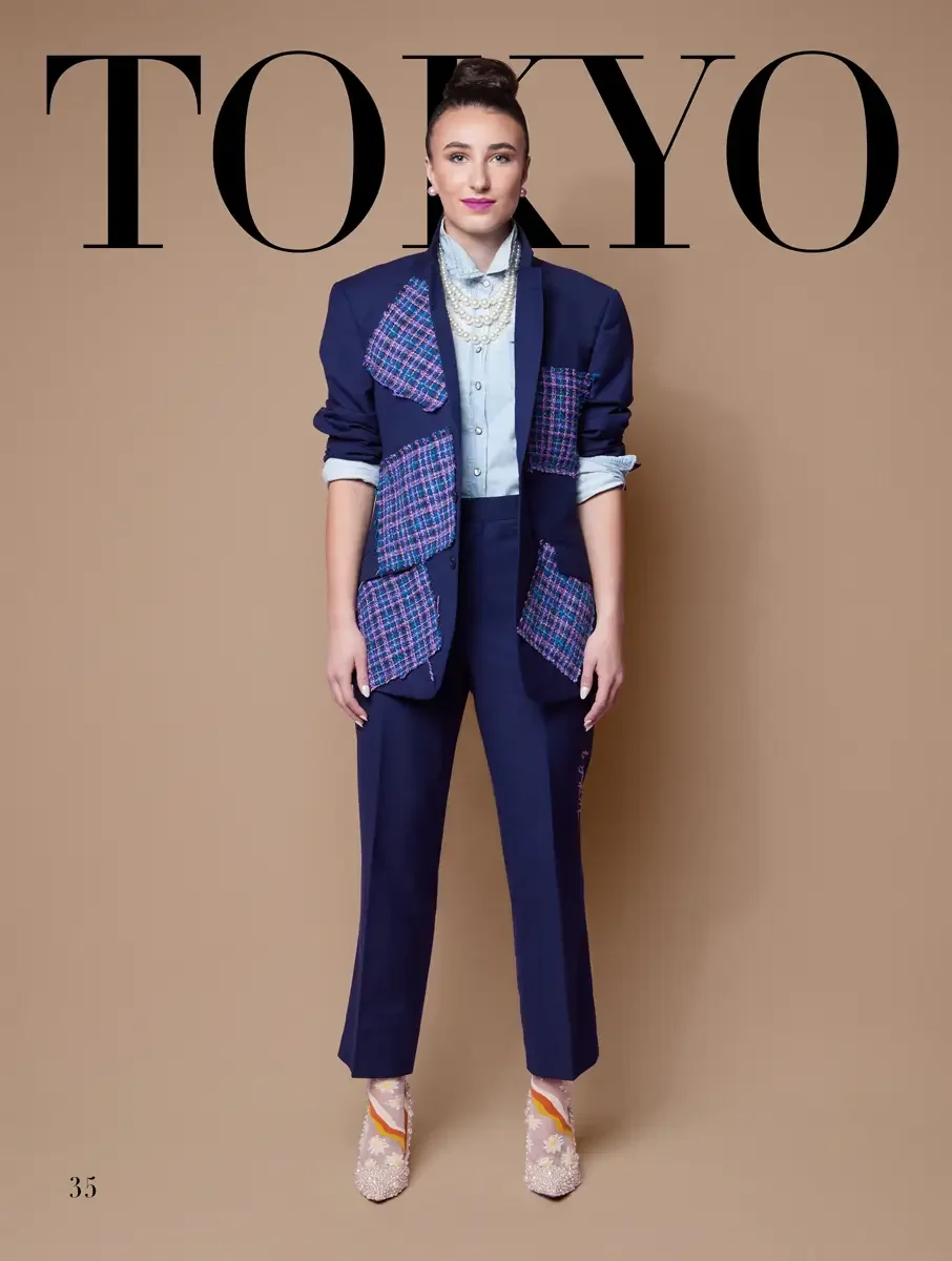 JUS10H 2025 Tokyo lookbook, a model wearing a navy blazer with colorful pink and blue tweed patchwork lapel and pocket panels, a light blue chambray button-down shirt, navy tailored trousers with subtle embroidery at the hem, layered pearl necklaces,