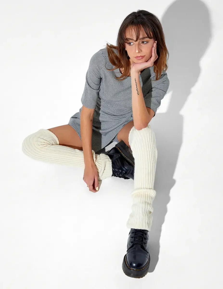 Model, full length, seated on floor, overhead angle, chin resting on hand, grey houndstooth mini dress with side buckle, cream ribbed leg warmers, black patent Dr. Martens platform shoes, New York studio test shoot, photographed by Scott Parker Photo