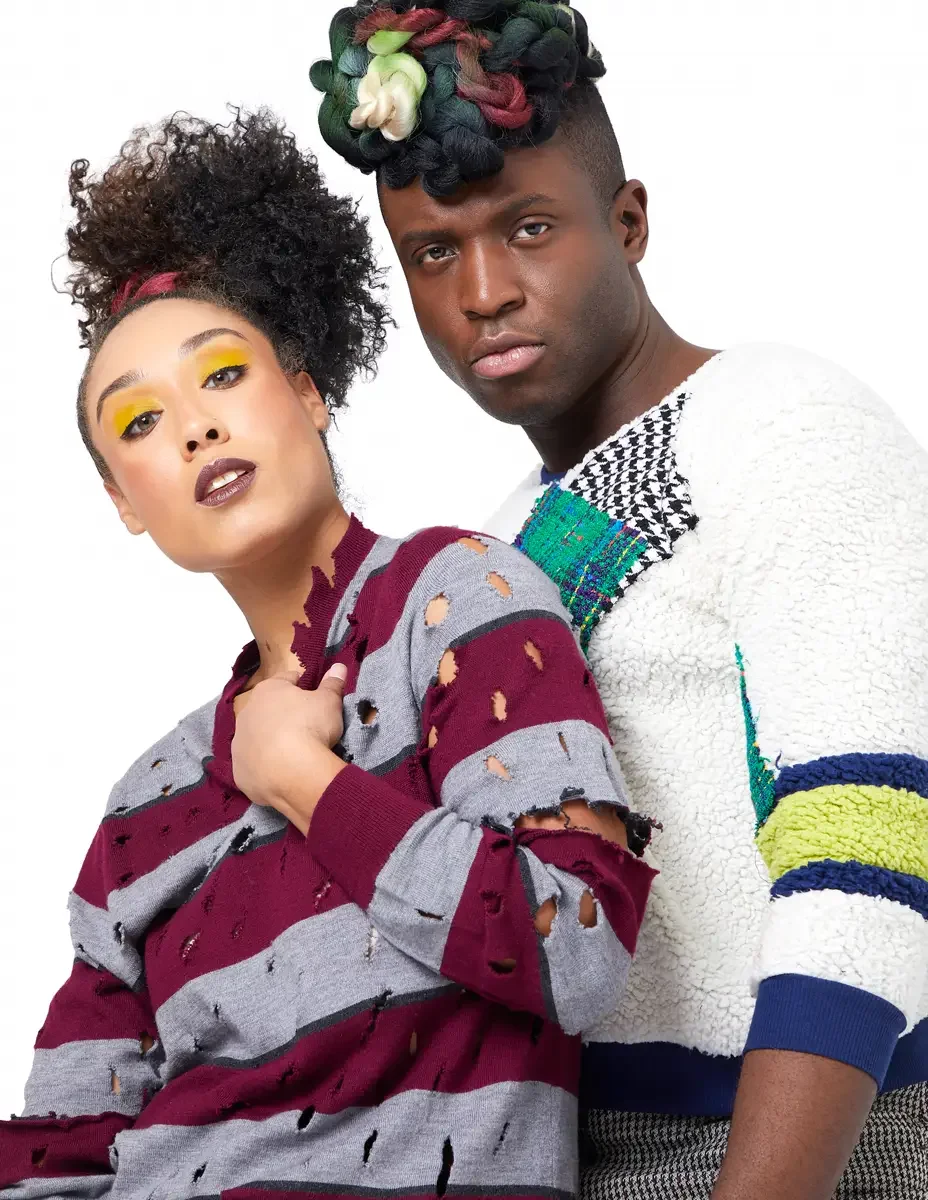 Model portfolio development session, high fashion editorial look, two models close together, woman in burgundy and heather grey destroyed-knit stripe sweater with hand at chest, man in white patchwork bouclé knit sweater with houndstooth and multicol