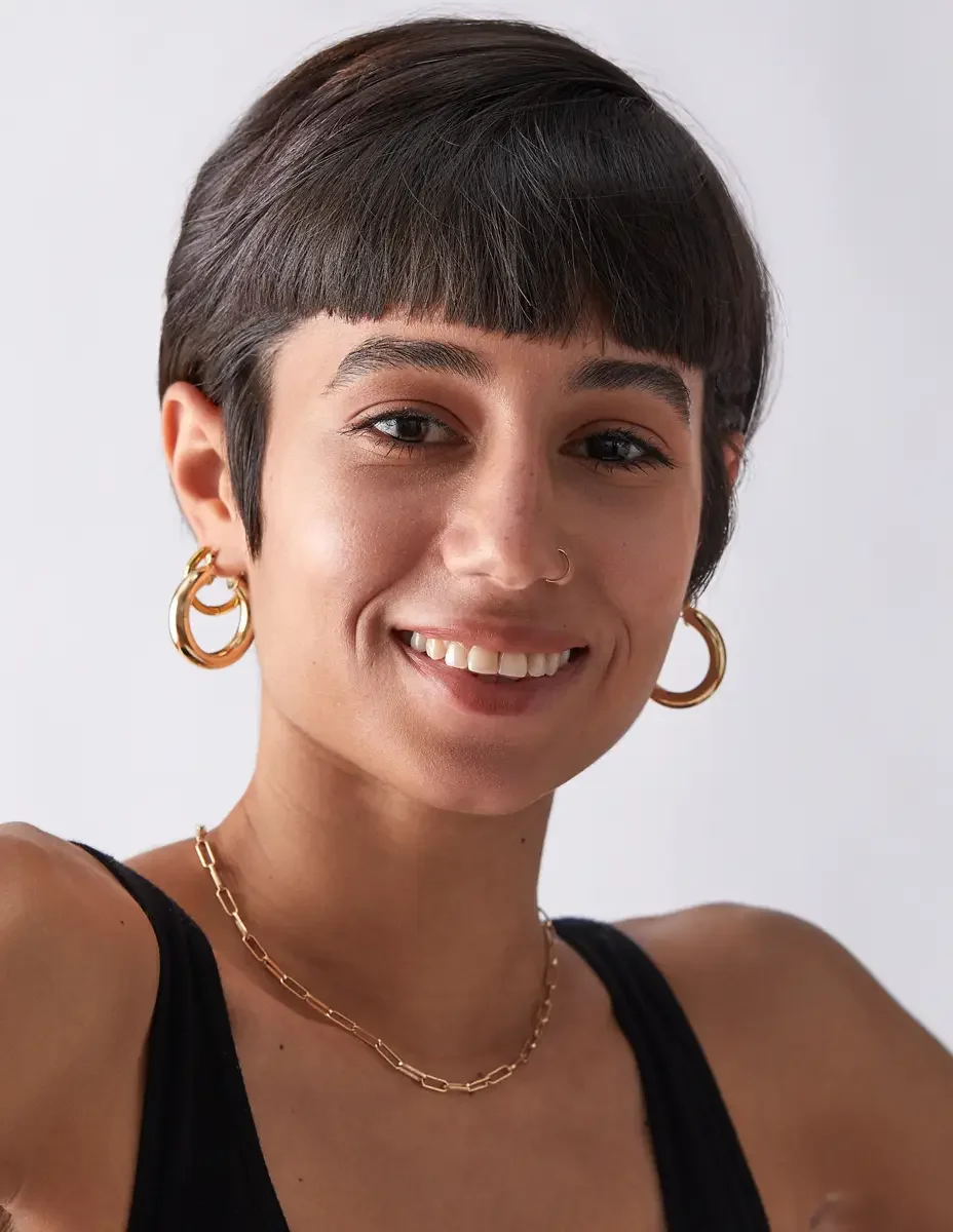Eloissa, smiling portrait, gold hoop earrings and chain necklace, pixie cut with blunt fringe, black tank, East Williamsburg studio test shoot, makeup by Schanica Pickens, photographed by Scott Parker Photo