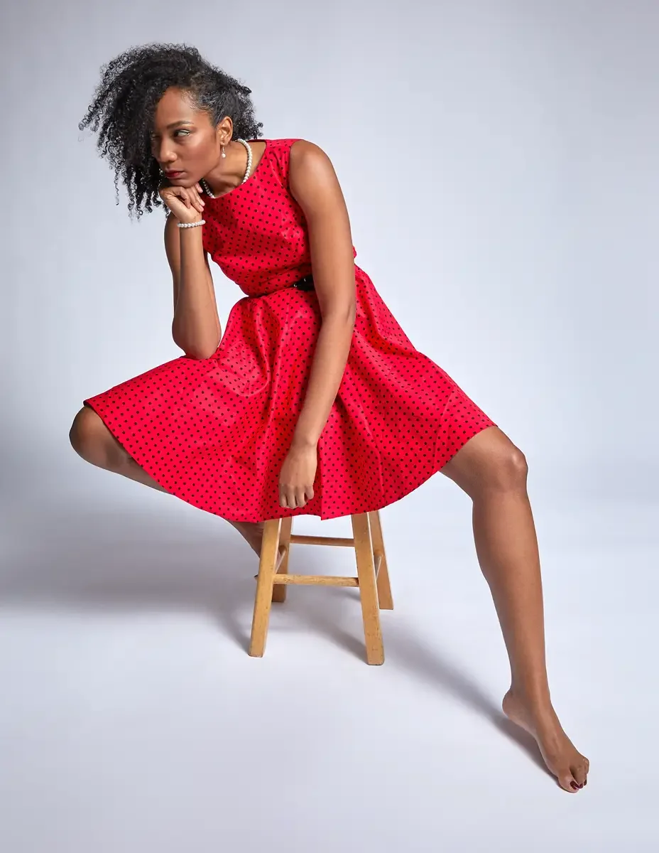 Arielle Chambers, seated on stool, red polka dot dress skirt spread wide, pearl necklace and earrings, East Williamsburg studio test shoot, makeup by Schanica Pickens, photographed by Scott Parker Photo