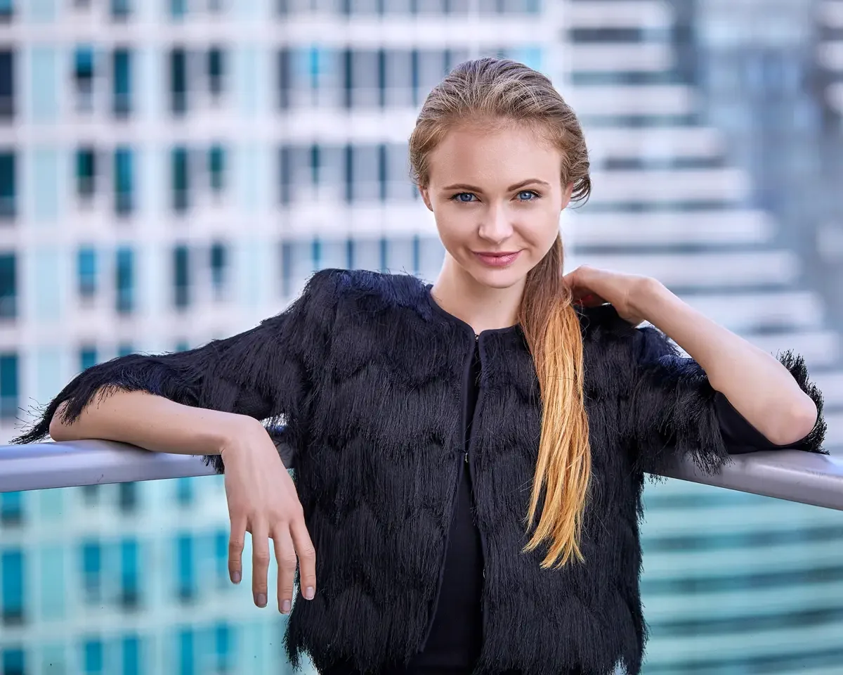 Julia, half length, leaning against the rooftop railing, black tiered fringe jacket with zip front over black fitted dress, hair slicked back in a low ponytail, Jersey City rooftop test shoot, photographed by Scott Parker Photo