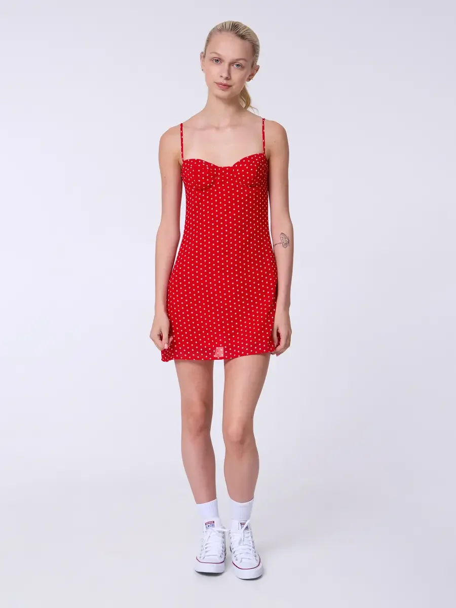 Model portfolio development session, commercial look, red polka dot sweetheart mini dress with spaghetti straps, full-length, facing camera, arms relaxed at sides, direct gaze, polka dot print and sweetheart bodice fully visible, white high-top Conve