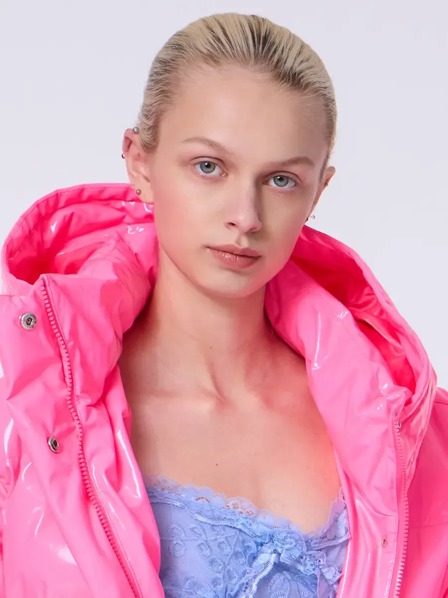 Model portfolio development session, commercial look, hot pink vinyl puffer jacket with hood framing face over periwinkle blue lace asymmetrical midi dress, close-crop, hair pulled back sleek, direct gaze, glossy vinyl hood surrounding face, lace dre