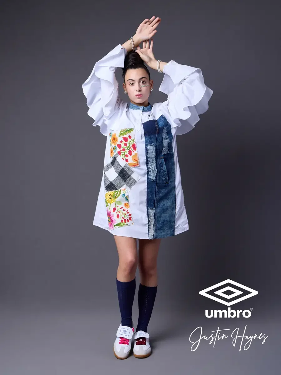 Fashion photographer producer and creative director work for the Umbro France collection. Vanessa standing with both arms raised overhead in an oversized white shirt dress with dramatic ruffled sleeves, a distressed denim center panel, and floral pat