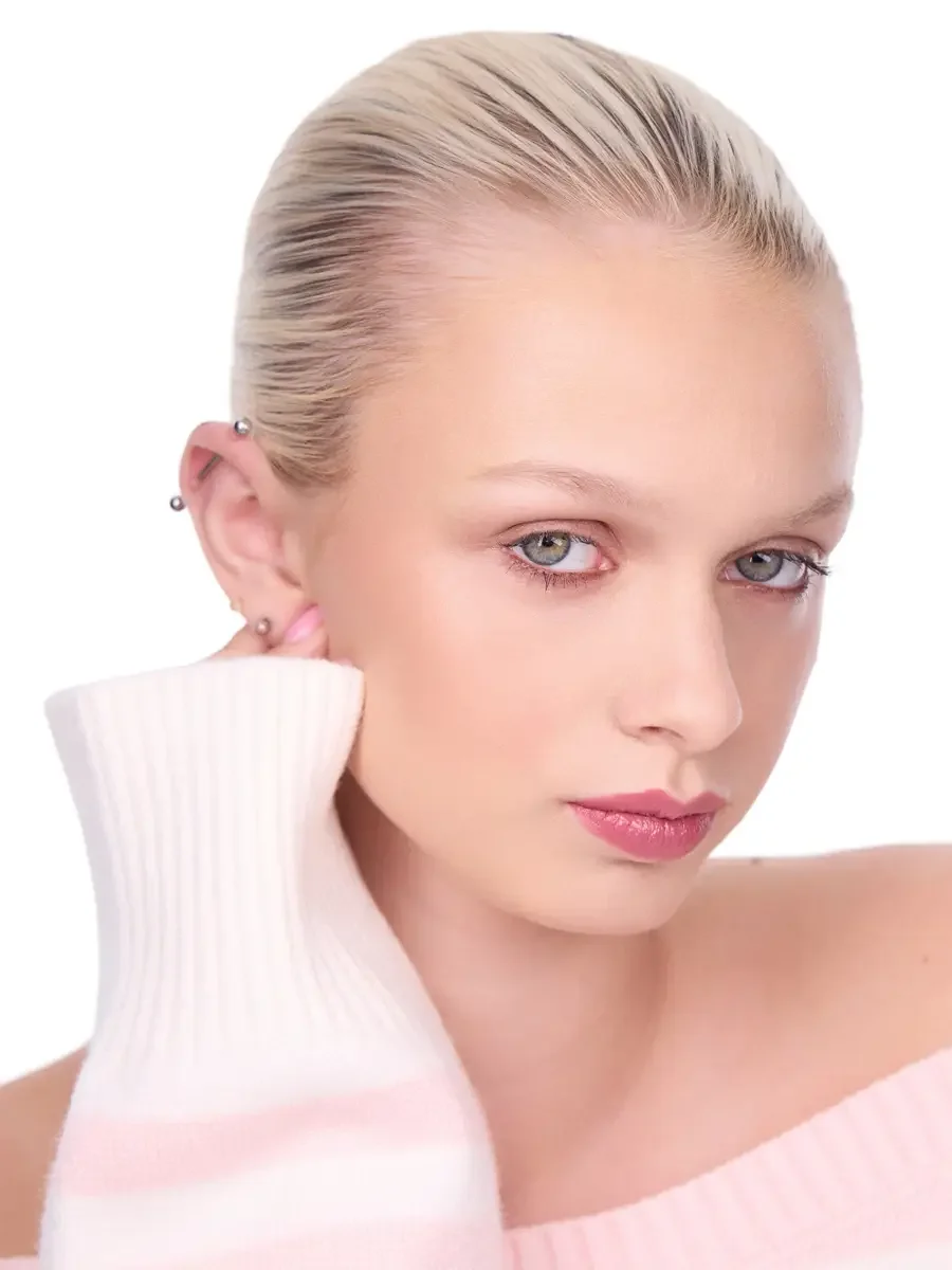 Model portfolio development session, beauty, close-crop, hair slicked back, profile turn, gaze forward, rose lip, soft eye, pink ribbed sweater held against ear, white background, photographed by Scott Parker Photo, New York