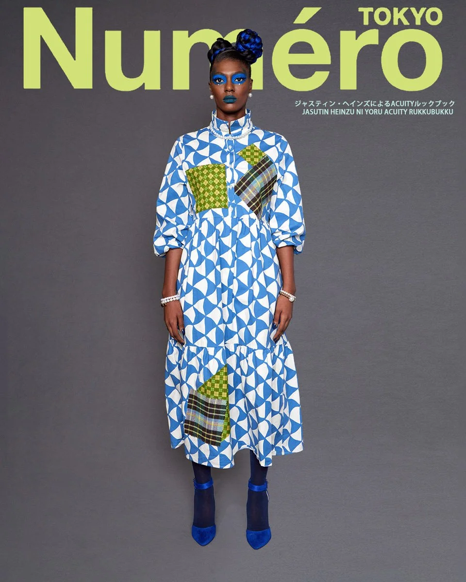 JUS10H by Justin Haynes ACUITY Collection lookbook for Numéro Tokyo by Scott Parker — model in blue and white geometric-print tiered midi dress with green checkered and tartan patchwork detail, pearl bracelets, navy tights, and cobalt blue suede pump