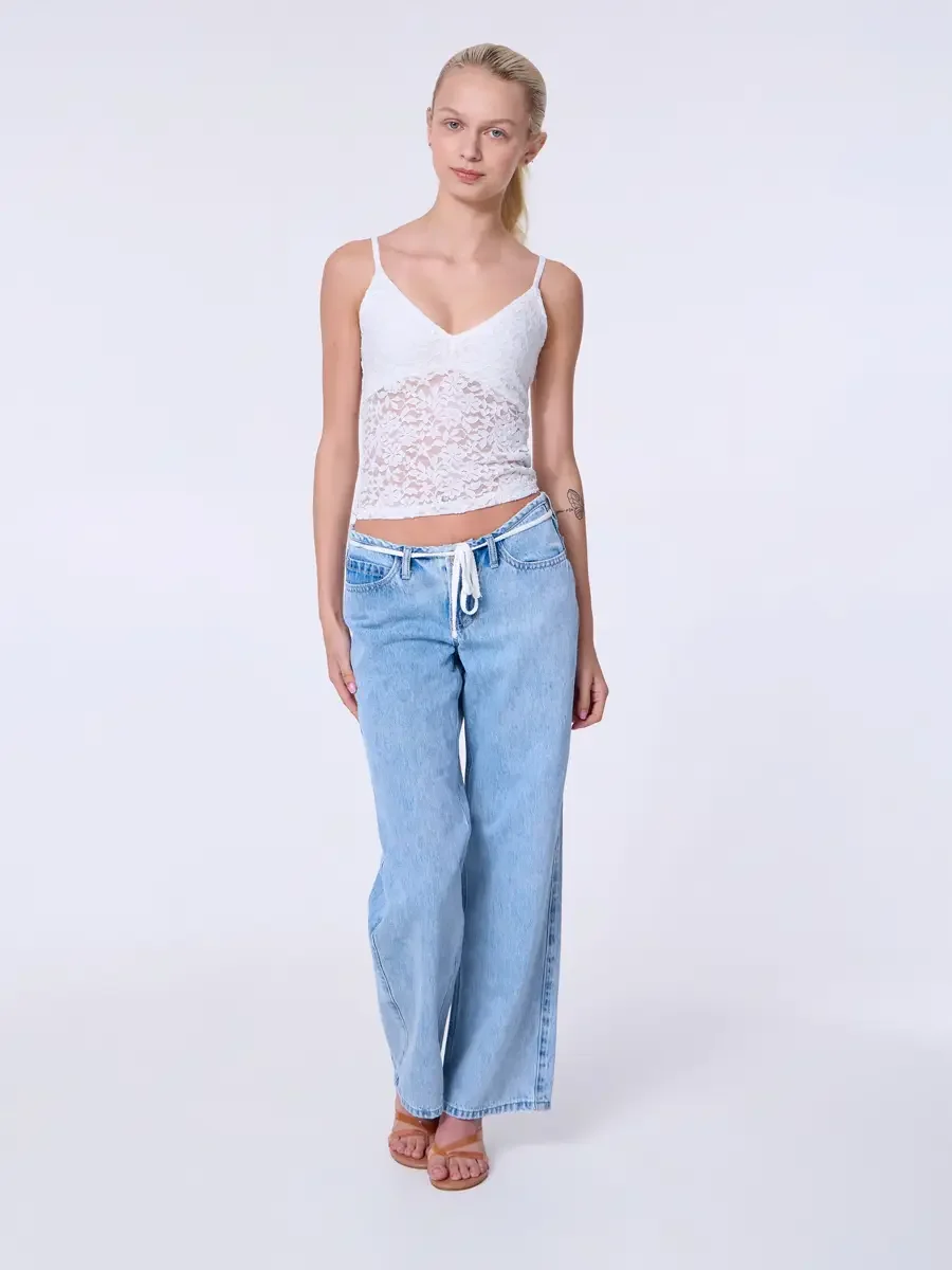 Model portfolio development session, commercial look, white lace crop camisole top and low-rise light wash wide-leg jeans with white drawstring detail, full-length, facing camera, arms relaxed at sides, neutral expression, tan strappy heeled sandals,