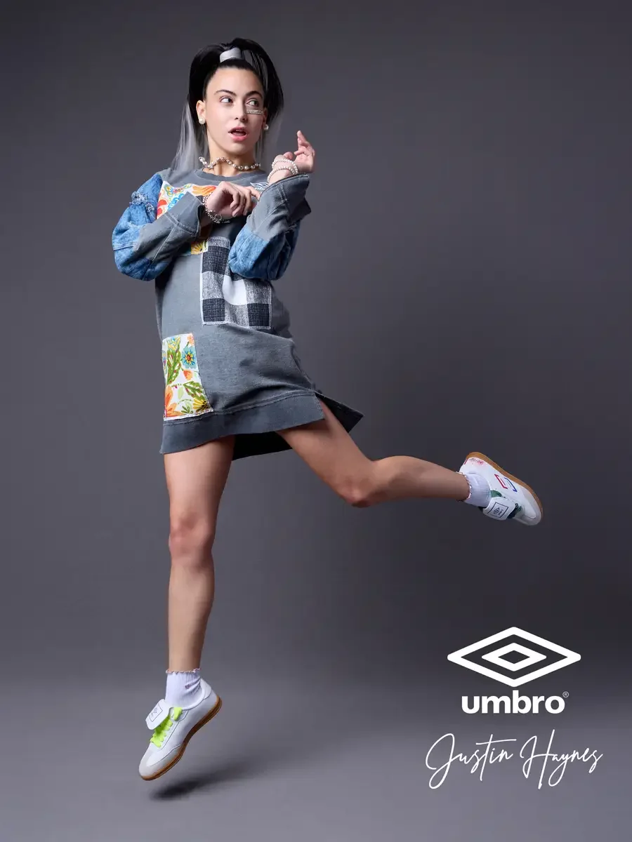 Summer 2026 Umbro France elevated soccer fan style. Vanessa leaping in a loose fit sweatshirt dress with floral and flannel patchwork panels and distressed denim sleeves by JUS10H, photographed in Springfield, Massachusetts, directed by Scott Parker 