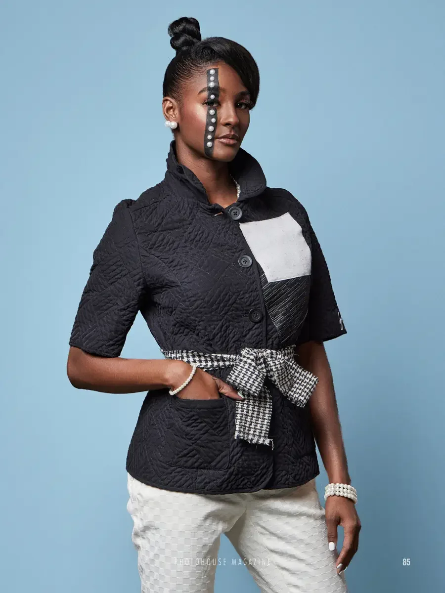 JUS10H 2025 Photohouse Magazine feature, model in black quilted short-sleeve jacket with white geometric patchwork panel and houndstooth sash belt over cream textured trousers, pearl bracelet, light blue background, photographed by Scott Parker Photo