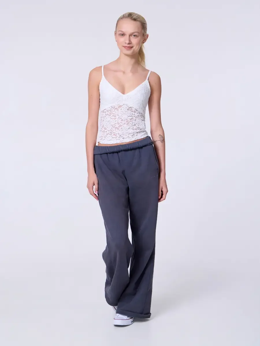 Model portfolio development session, commercial look, white lace crop camisole top and wide-leg charcoal sweatpants with elastic waistband, full-length, facing camera, mid-stride pose, soft smile, sweatpant leg caught in motion, white Converse sneake
