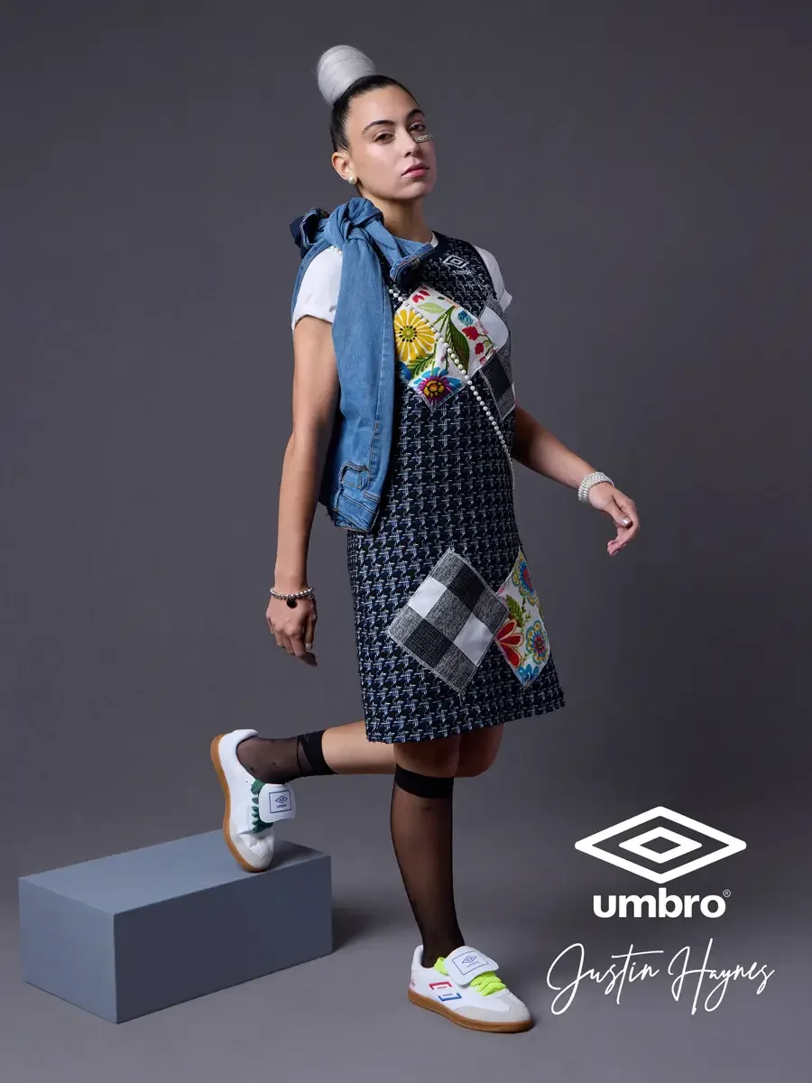 Fashion photographer in Massachusetts for the Umbro France collection. Vanessa in a side profile stance with one foot raised and a denim jacket draped over her shoulders, wearing a navy houndstooth sleeveless shift dress with diagonal floral and patc