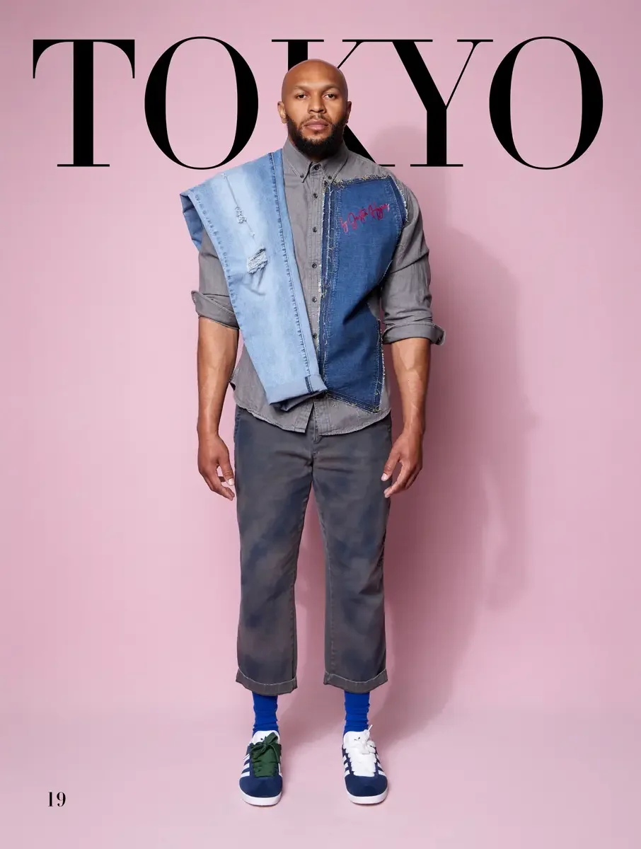 JUS10H 2025 Tokyo lookbook, two-tone patchwork denim vest worn over grey button down shirt and grey cropped trousers with blue Adidas sneakers, pink background, photographed by Scott Parker Photo for the Tokyo Fashion Council