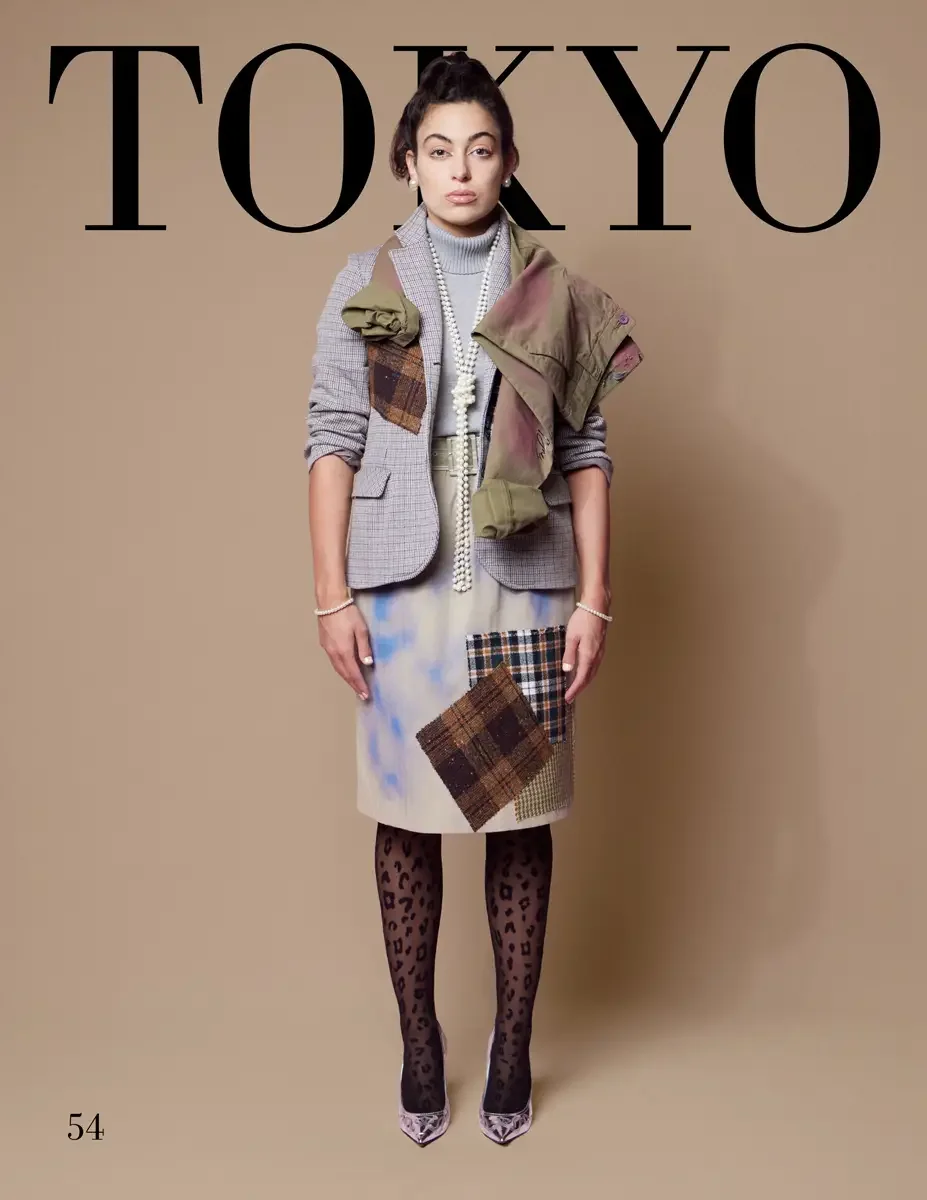 JUS10H 2025 Tokyo lookbook, a female model wearing a gray micro-check blazer with brown plaid patchwork appliqués and a large olive military jacket draped over one shoulder, a gray turtleneck sweater, a cloud-dyed ivory pencil skirt with dark brown a
