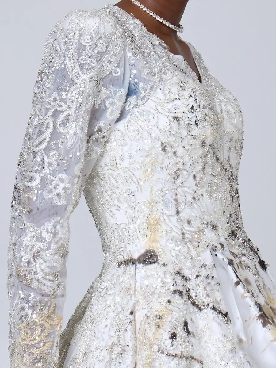 JUS10H 2025 New York Bridal Fashion Week, side-profile close detail of white silver-beaded lace ball gown bodice with full-coverage pearl and crystal embroidery, sheer beaded lace sleeve, and diamond choker, transitioning into an abstract paint-splat