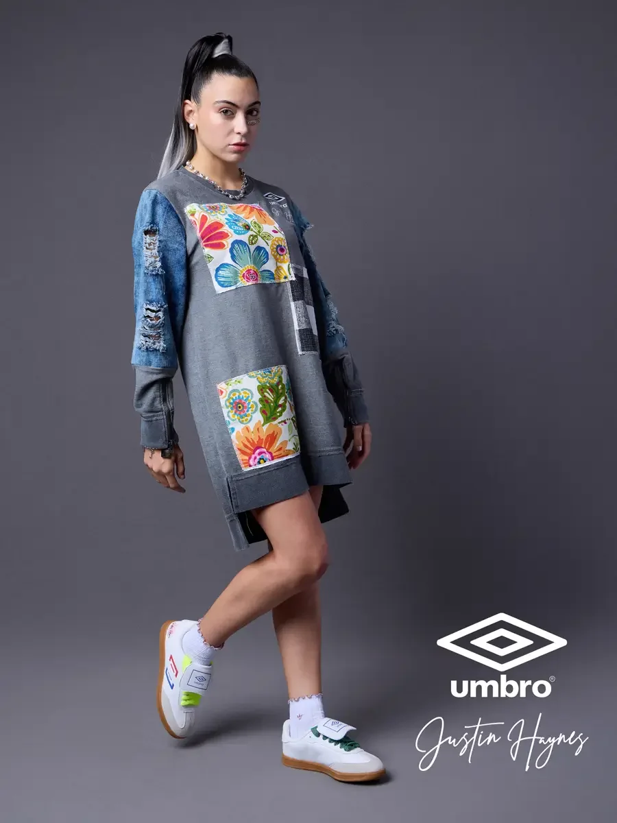 Fashion brand photography for the Umbro France collection. Vanessa in a side-stepping stance in an oversized acid-washed sweatshirt dress with floral patchwork panels and distressed denim sleeves, styled by Justin Haynes, model Vanessa directed by Sc