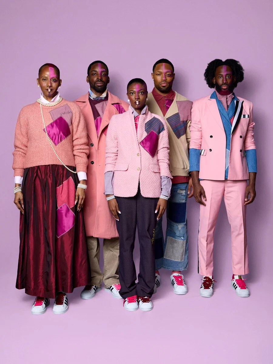 Five individuals standing against a pink background, dressed in colorful, coordinated fashion with pink and purple accents, wearing sneakers, with rainbow and purple face paint.