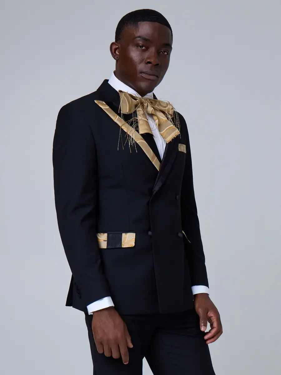 JUS10H 2025 New York Bridal Fashion Week, black double-breasted tuxedo with gold jacquard lapels, oversized gold jacquard bow tie with feather detail, and matching pocket square and pocket trim, photographed by Scott Parker Photo