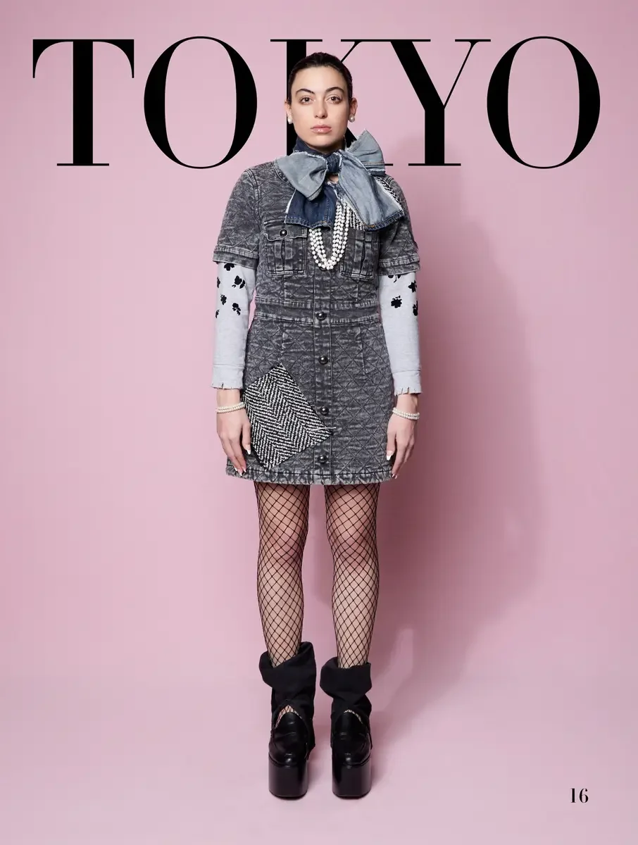 JUS10H 2025 Tokyo lookbook, acid wash grey denim mini dress with herringbone patch and denim bow over floral sleeve top with fishnet tights and platform boots, pink background, photographed by Scott Parker Photo for the Tokyo Fashion Council