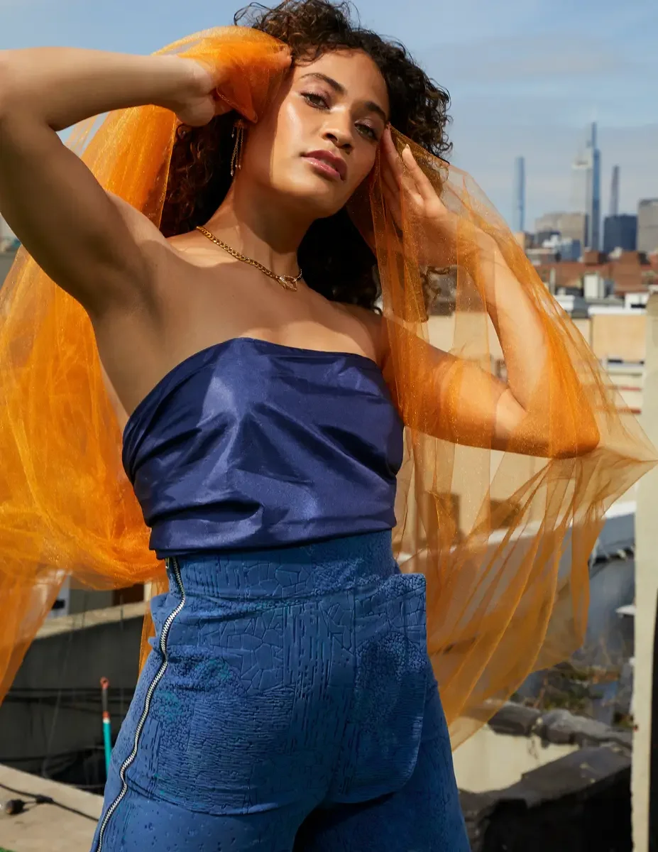 Fashion test shoot, model Ireland T in Amy Page DeBlasio textured blue wide-leg pants with zipper detail and navy strapless top, orange tulle framing face, East Village rooftop, New York City, styling by Matsine Stinson, makeup by Stefani Paige Vivia