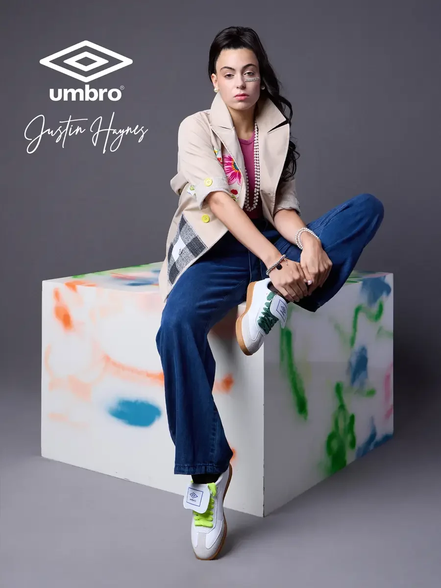 Fashion photographer in Massachusetts for the Umbro France collection. Vanessa seated on a color-splashed prop with one leg raised in a sand utility jacket with floral patchwork panels over a fuchsia t-shirt and wide-leg dark indigo jeans, styled by 