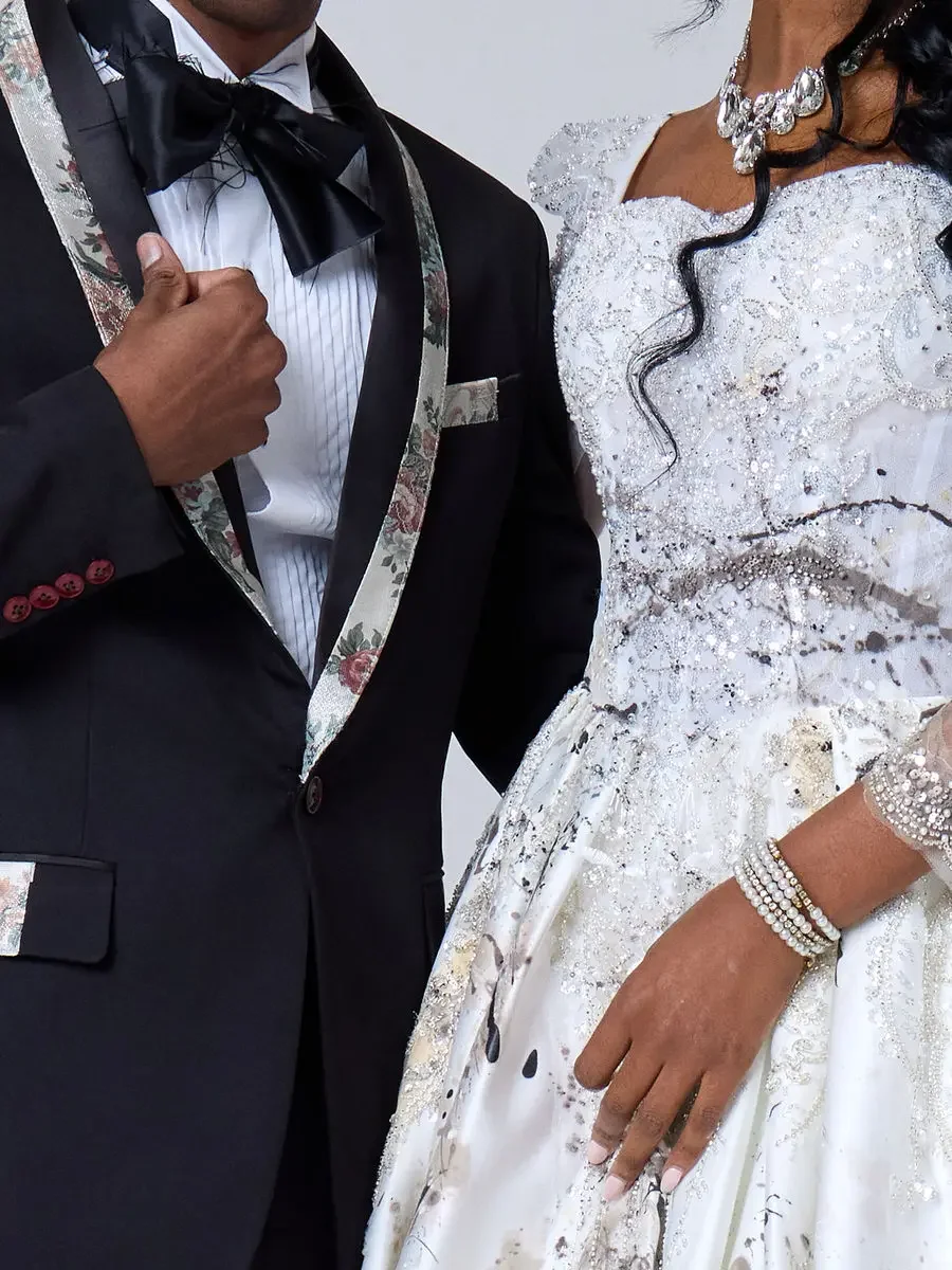 JUS10H 2025 New York Bridal Fashion Week, detail of black tuxedo with floral-print shawl lapels, black satin bow tie, and matching pocket square alongside white beaded paint-splatter ball gown with crystal waist belt and stacked pearl and crystal bra
