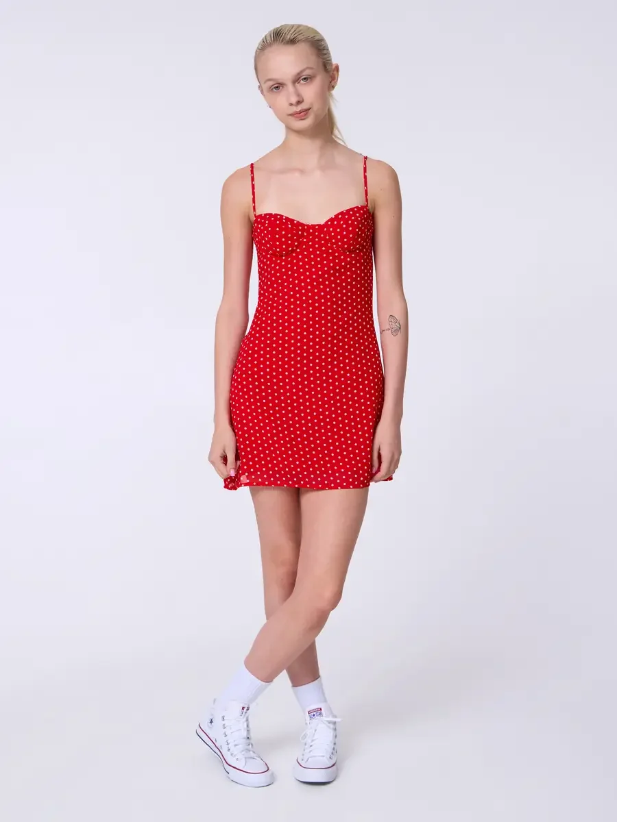 Model portfolio development session, commercial look, red polka dot sweetheart mini dress with spaghetti straps, full-length, slight turn to camera, arms relaxed, weight shifted to one hip, soft expression, dress silhouette and polka dot print shown 