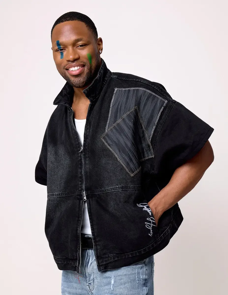 JUS10H Black Summer Jacket editorial, three-quarter portrait of male model in black denim wide-shoulder zip jacket with gray patchwork panels, smiling, light-wash jeans, white background, photographed by Scott Parker Photo