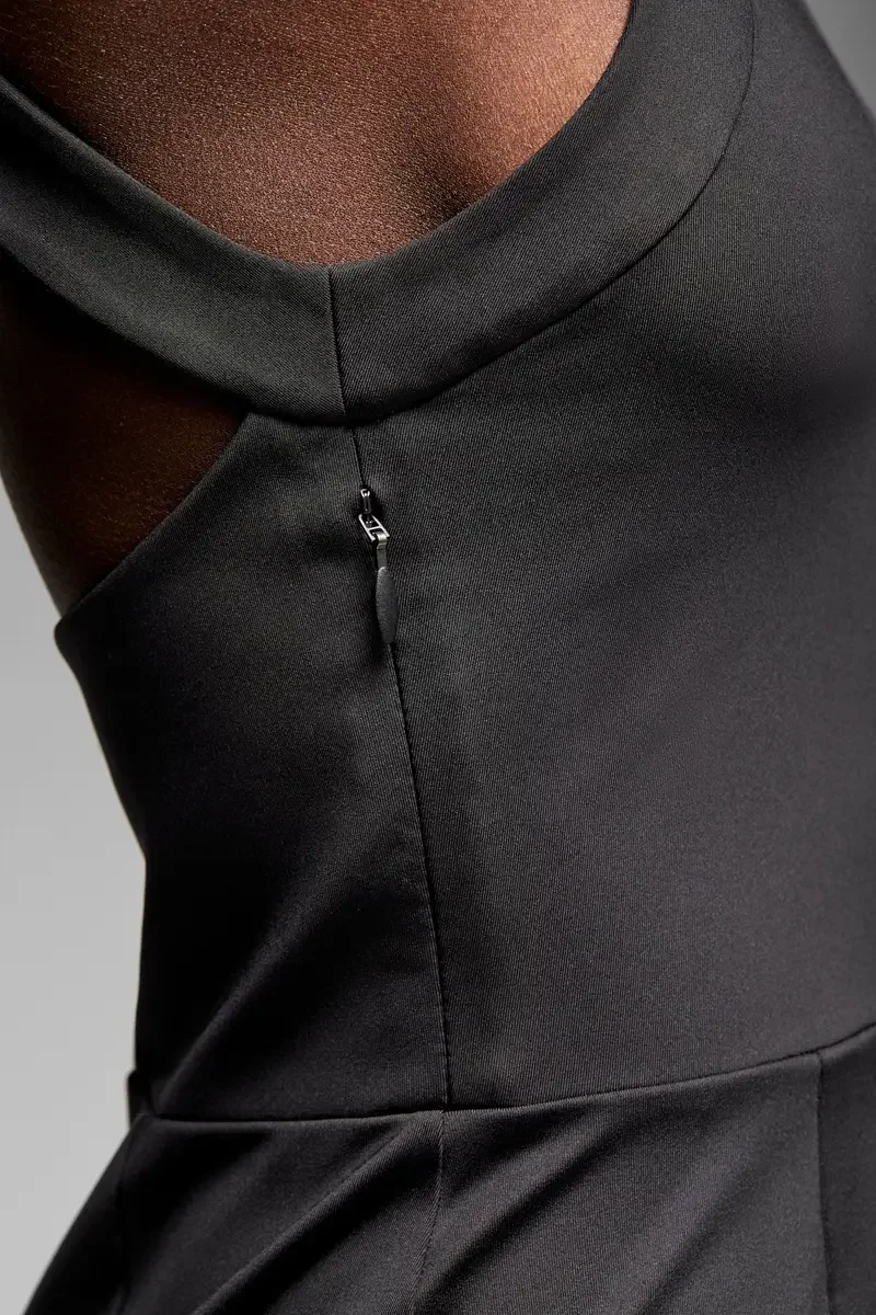 Minika Ko lookbook, detail, black halter-neck dress, close view of round neckline, diagonal strap seam, center-front zipper pull, and horizontal waist seam, smooth matte-finish semi-water-repellent synthetic, gray background, photographed by Scott Pa
