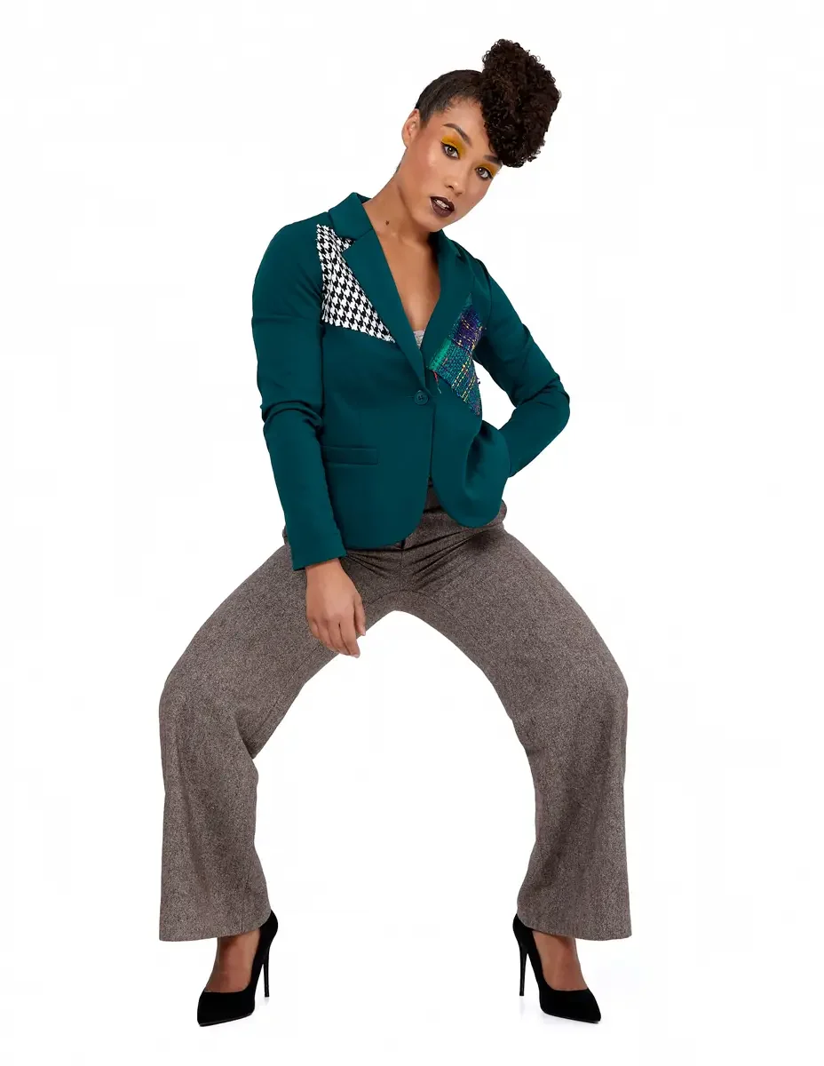 Model portfolio development session, high fashion editorial look, teal single-button blazer with houndstooth and multicolor tweed appliqué panels, wide-leg heathered orange trousers, black stiletto heels, full-length, deep squat with head tilted, int