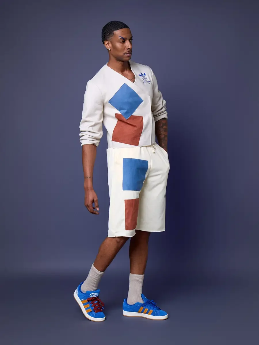 JUS10H x Adidas Brasil campaign, model in profile walking stance, white patchwork long-sleeve top with blue and terracotta suede panels over cream patchwork shorts, Adidas Campus 00s in royal blue suede with orange stripes, periwinkle background, pho
