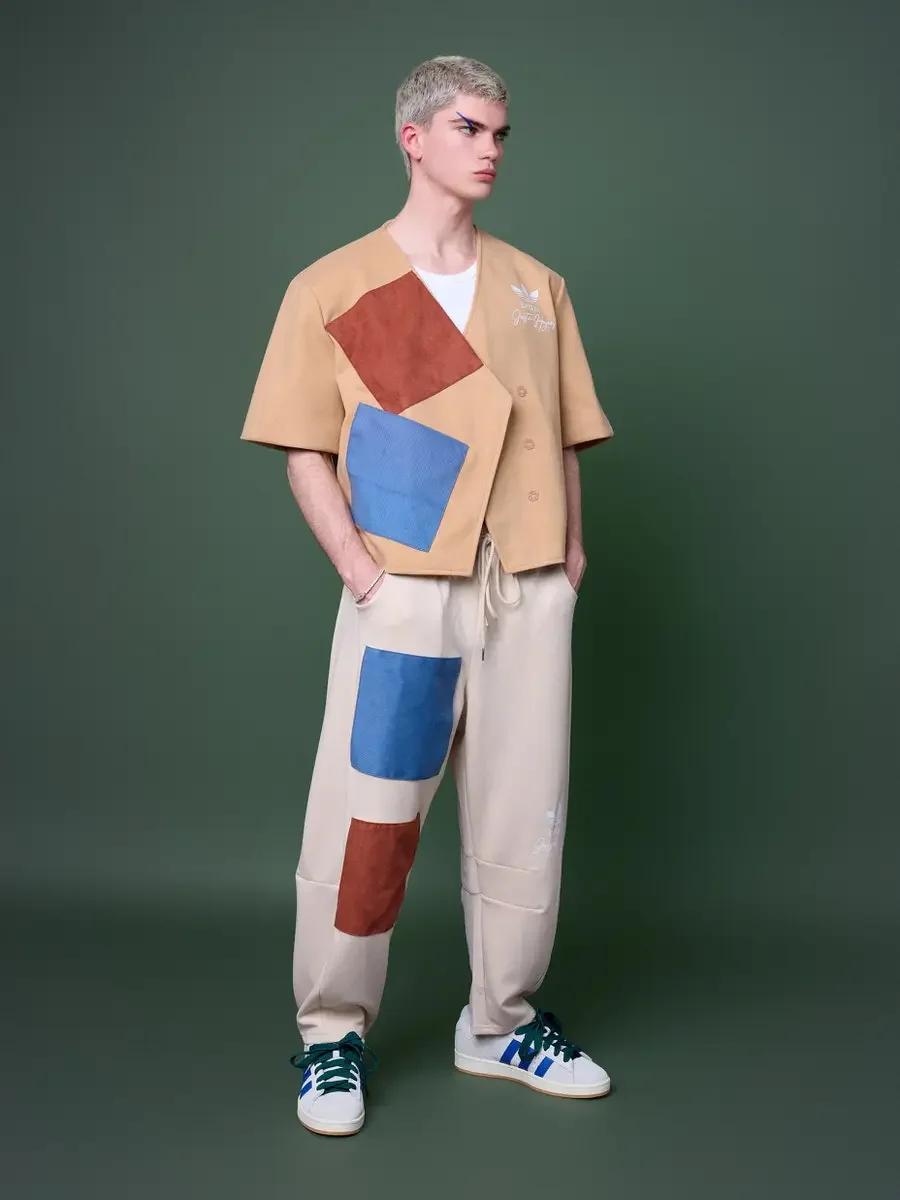 JUS10H x Adidas Brasil campaign, full-length standing shot looking left, tan patchwork short-sleeve vest with terracotta and blue suede panels over cream wide-leg patchwork trousers, Adidas Campus 00s in white with blue stripes and dark green laces, 