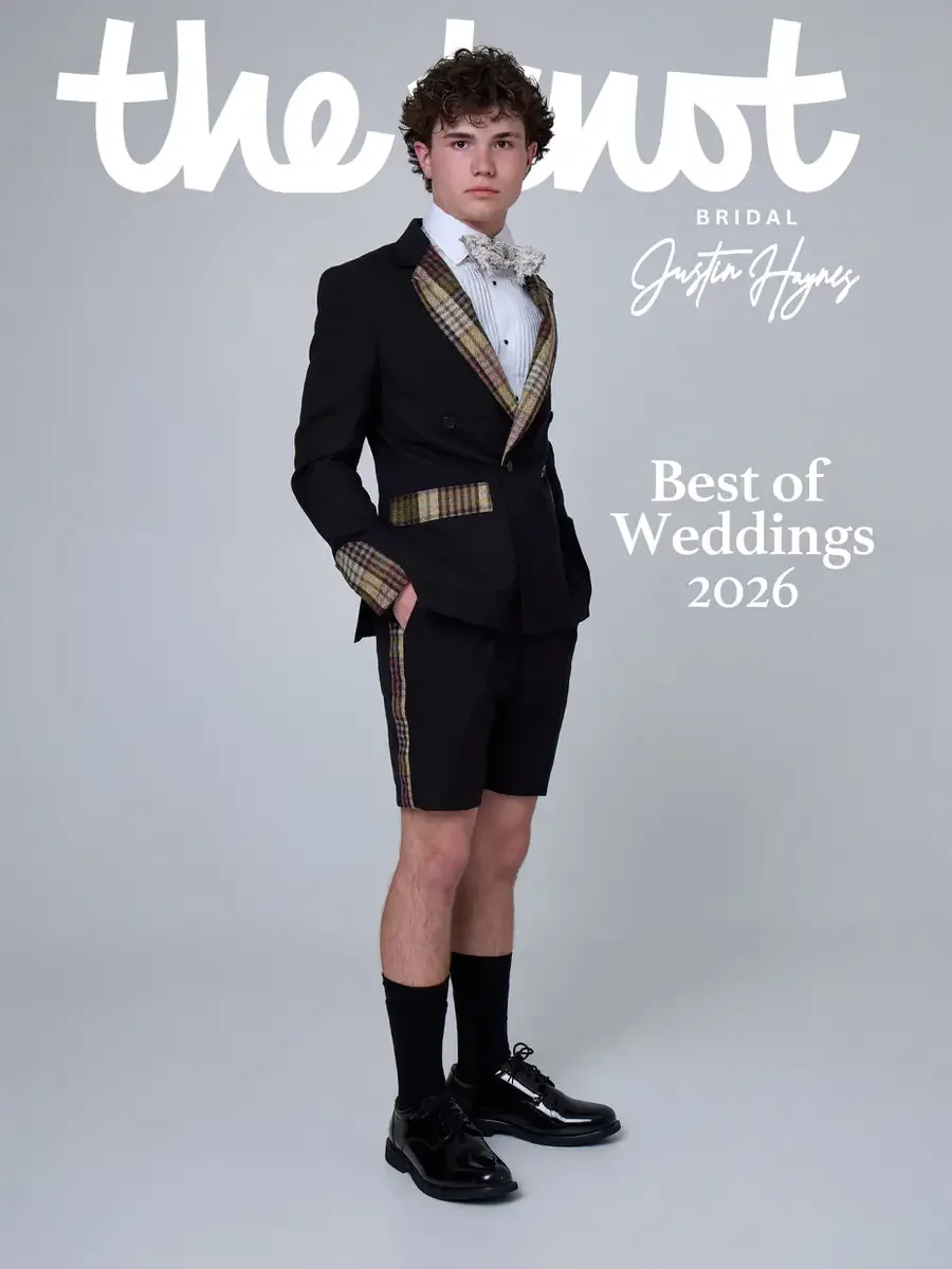 JUS10H 2025 The Knot Bridal feature, Justin Haynes Best of Weddings 2026 cover, black shorts suit with plaid lapels, pocket trim, cuffs, and side stripe, styled with a white lace bow tie, black dress socks, and patent leather oxfords, photographed by