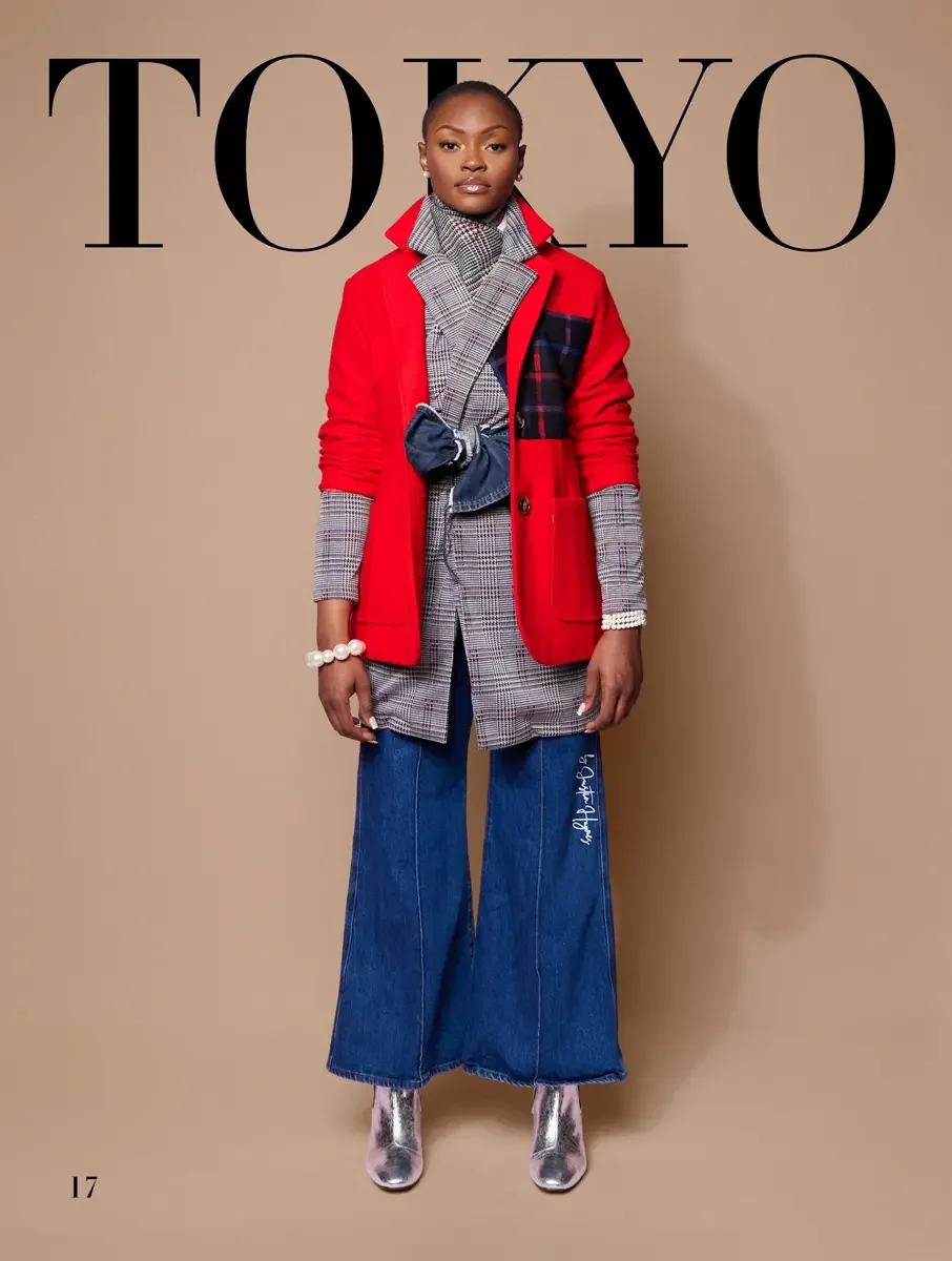 JUS10H 2025 Tokyo lookbook, bold red blazer with tartan patch over glen plaid longline jacket and wide leg blue denim trousers with silver boots, tan background, photographed by Scott Parker Photo for the Tokyo Fashion Council