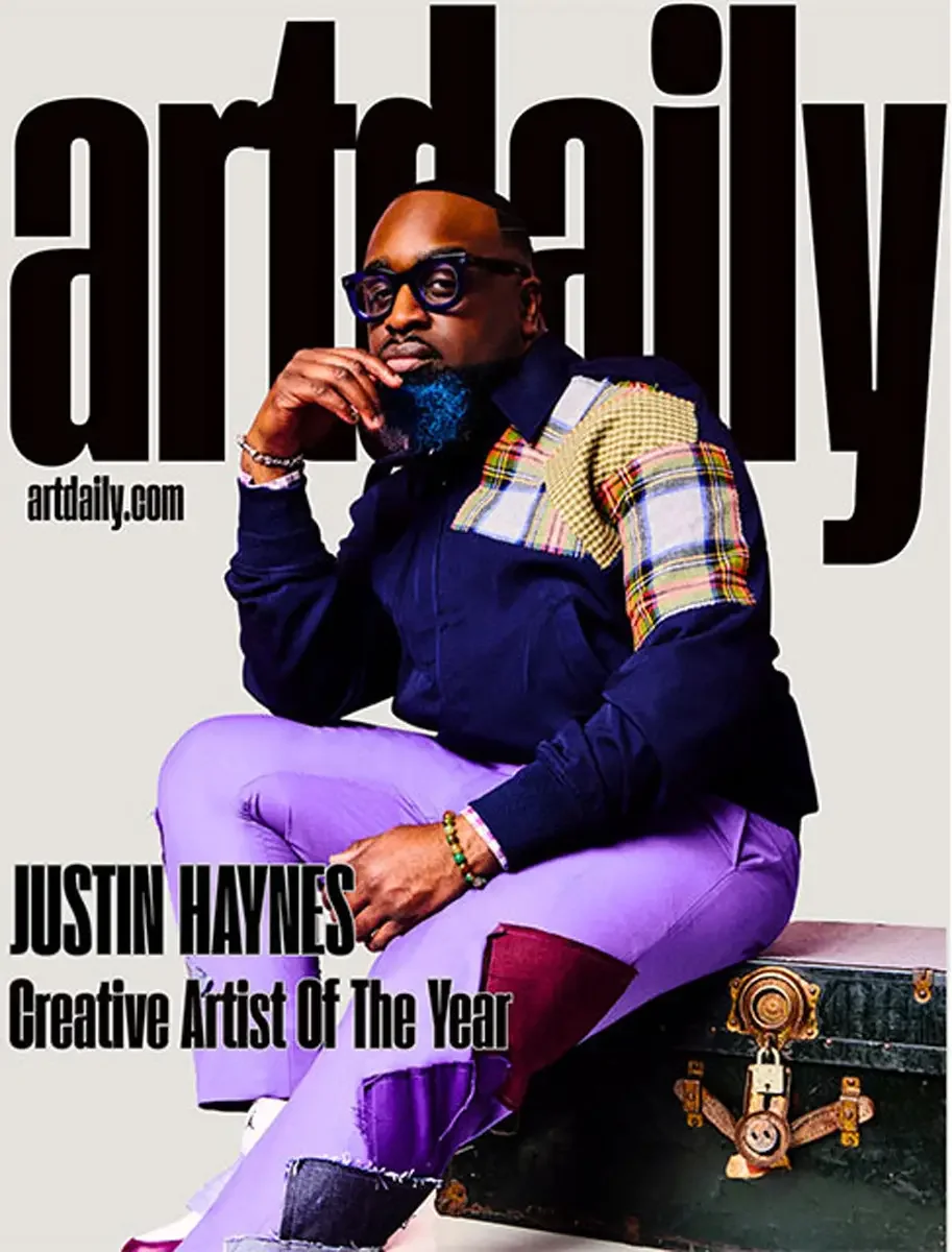 JUS10H 2025 artdaily feature, Creative Artist of the Year, seated editorial portrait, navy and plaid patchwork jacket, purple trousers, photographed by Scott Parker Photo