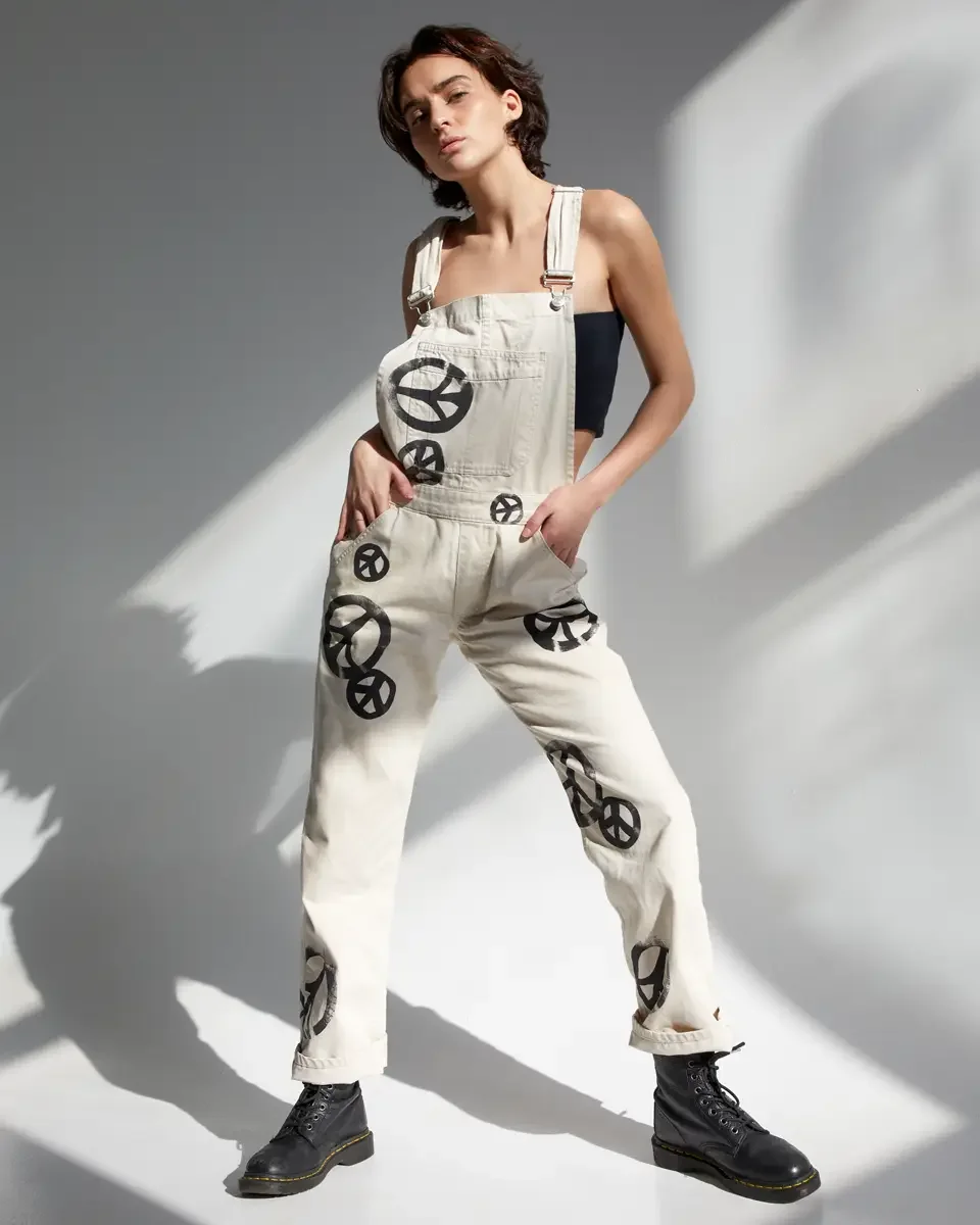 Tess, full-length, hand in pocket, cream canvas overalls with allover hand-painted black peace sign print, black strapless bandeau top, black lace-up Dr. Martens boots, New York studio test shoot, makeup by Schanica, photographed by Scott Parker Phot