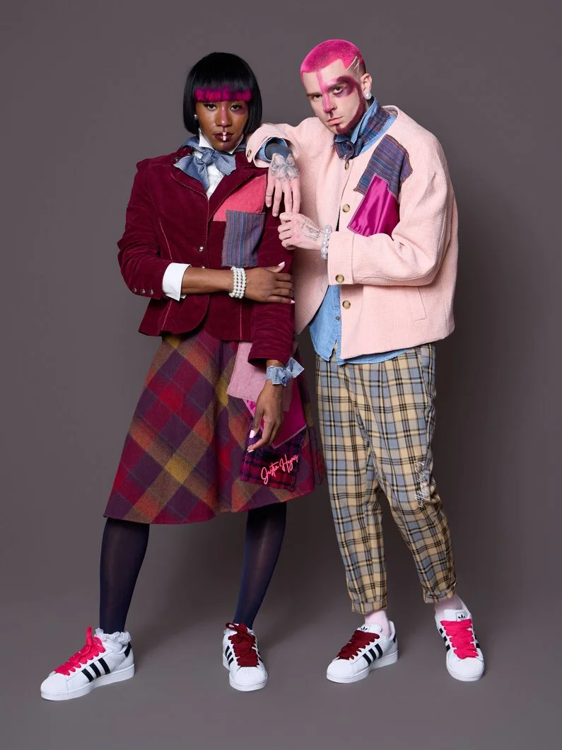 Two people standing against a gray background, dressed in colorful and eclectic fashion styles.