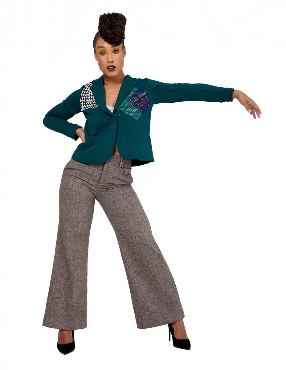 Model portfolio development session, high fashion editorial look, teal single-button blazer with houndstooth and multicolor tweed appliqué panels, wide-leg heathered trousers, black stiletto heels, full-length, one arm extended outward, wide stance, 