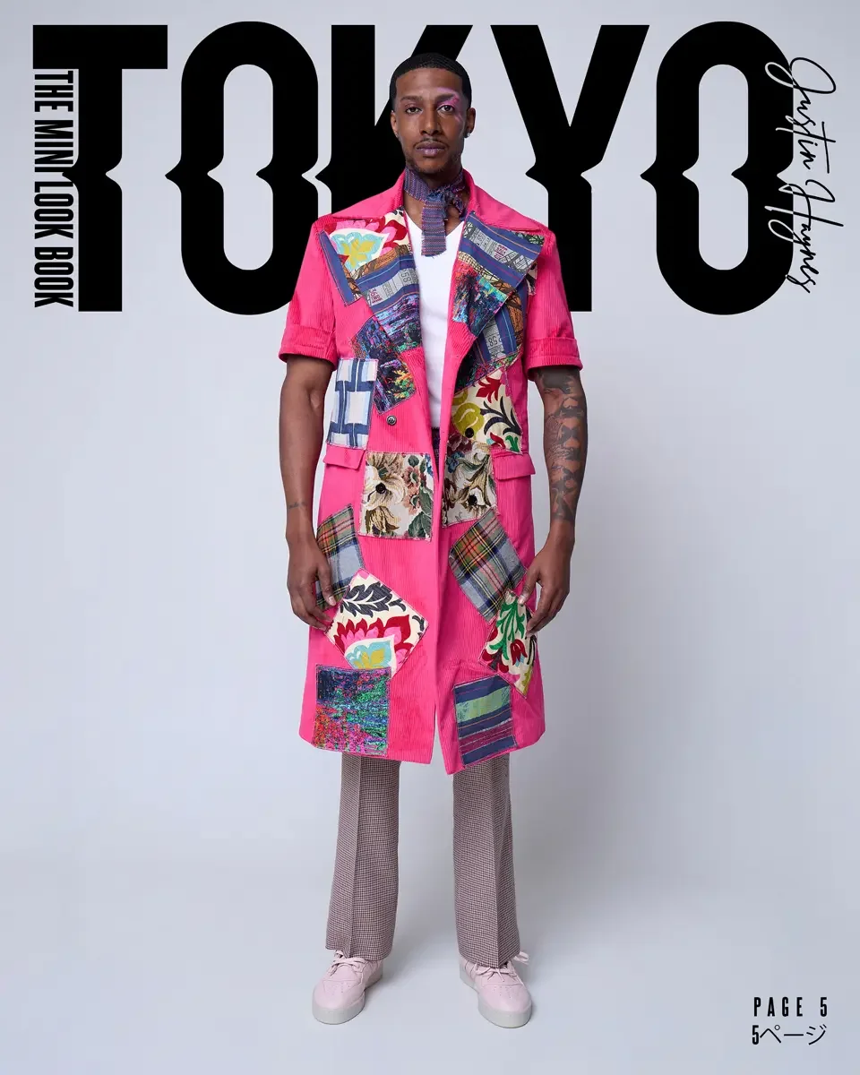 Man wearing a colorful patchwork coat with pink as the dominant color, standing in front of the words 'TOYO' and 'Justin Harnby'.