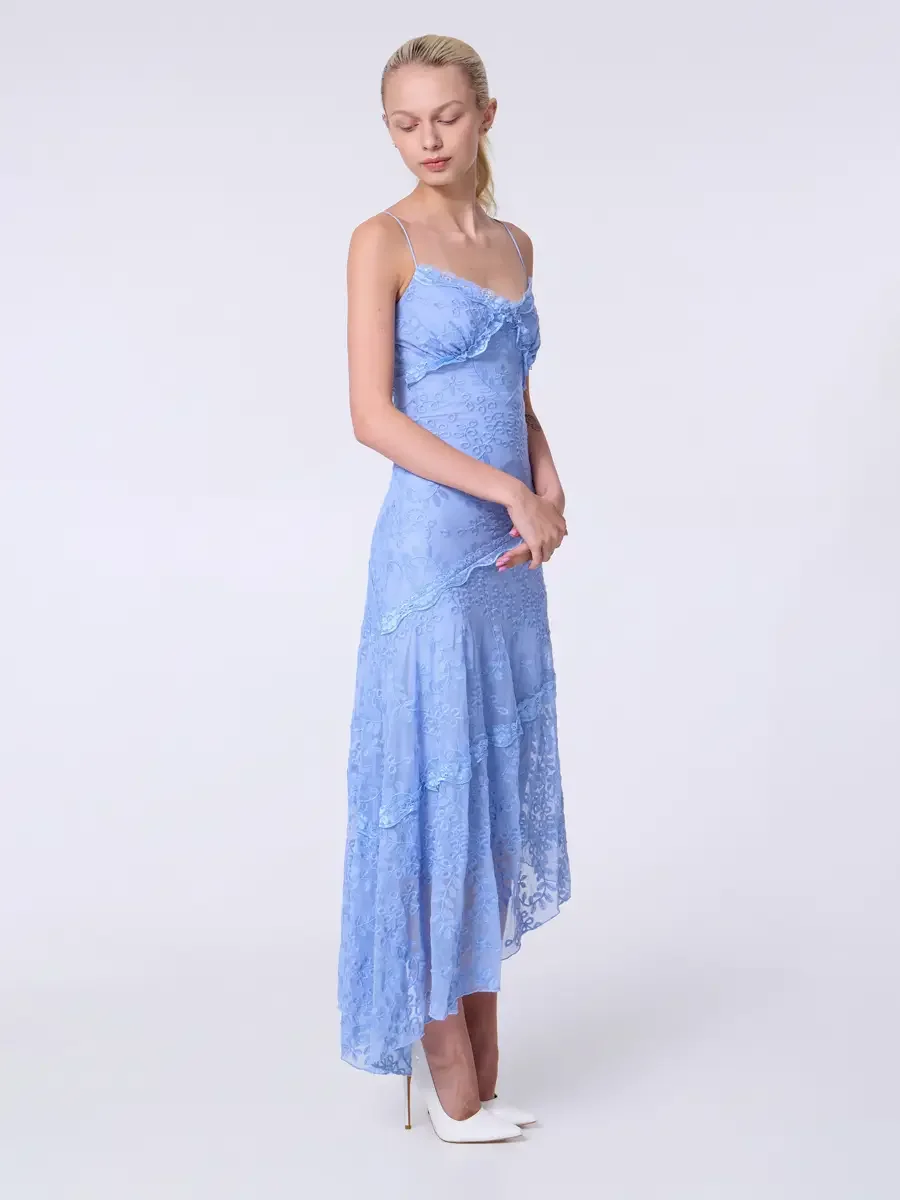 Model portfolio development session, commercial look, periwinkle blue lace asymmetrical midi dress with ruffle bodice detail and spaghetti straps, full-length, three-quarter turn, gaze downward, hands loosely clasped at front, asymmetrical hem at ful